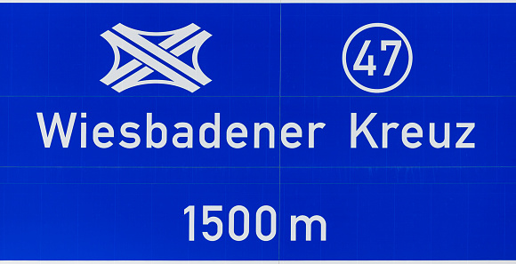 Daytime close-up of a blue roadsign on German Autobahn A3 near Frankfurt airport, directing to the interchange at Wiesbaden, the 'Wiesbadener Kreuz'