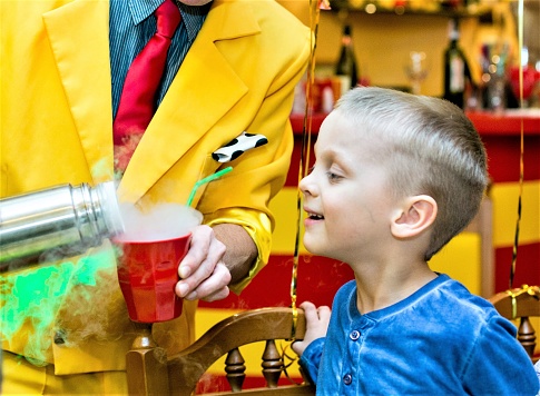 cute little boy in a blue shirt looks at a magician who shows a trick