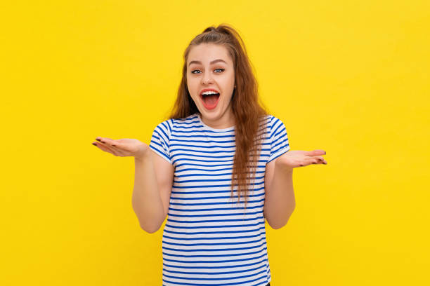 istock Amazed and impressed girl with brown-haired expressing wonder with gesturing hands up, say wow, stands in white-blue striped t shirt over yellow background 1409856236