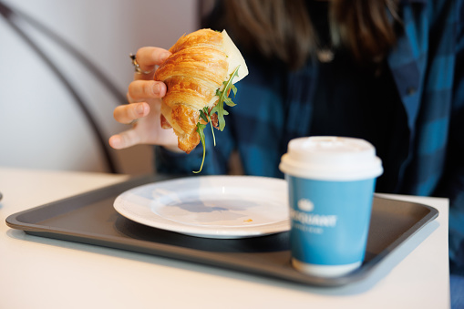 Eating sandwich croissant in cafeteria in the city, paper coffee cup on a tray, street food and drinks