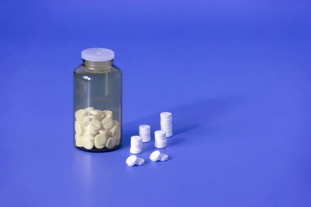 White pills, medical tablets, placebo or vitamins and brown transparent bottle with medicine on dark blue background closed up, vertical plane, copy space on the right Medicine, pharmacy statin photos stock pictures, royalty-free photos & images