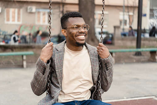 Portrait of a happy African American young man swinging on the playground and enjoying