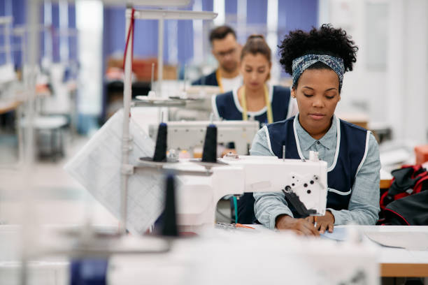 African American dressmaker working at production line in a factory. Young African American woman sewing while working as seamstress at clothing factory. clothing design studio stock pictures, royalty-free photos & images