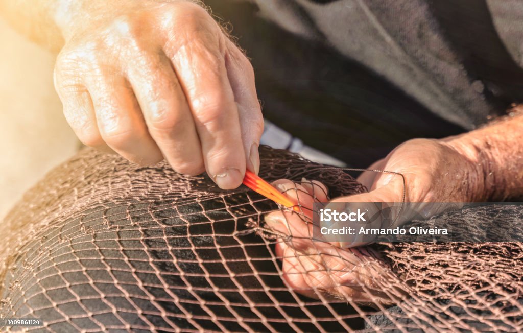 Senior fisherman repairs a fishnet by hand with a needle - Traditional fishing industry concept Senior fisherman repairs a fishnet by hand with a needle - Traditional fishing industry concept. Fisherman Stock Photo