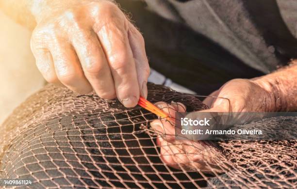 Senior Fisherman Repairs A Fishnet By Hand With A Needle Traditional Fishing Industry Concept Stock Photo - Download Image Now
