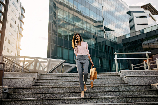 Beautiful brunette business woman walking down the stairs while talking on the phone and carrying laptop bag