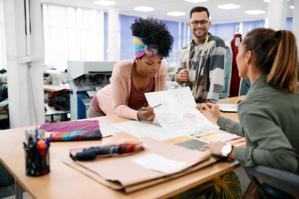 Young fashion designers analyzing sketches of their new clothing line in a studio. African American clothing designer and her colleagues working on new ideas in fashion design studio. fashion designer stock pictures, royalty-free photos & images