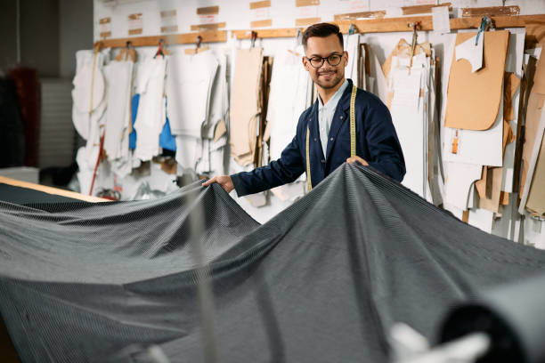若い幸せな繊維労働者は、仕立て屋で働いている間に布地を広げます。 - unrolling ストックフォトと画像