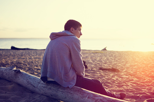 Toned Photo of Pensive Young Man on the shore at the Sunset