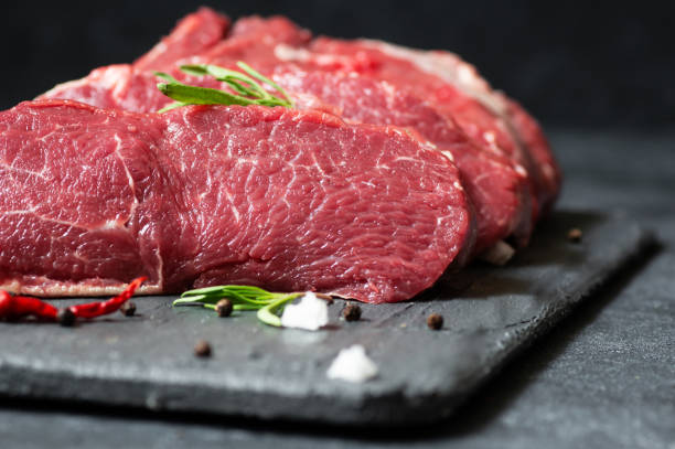 Raw beef steak meat on stone board with thyme and peppers, butcher concept stock photo