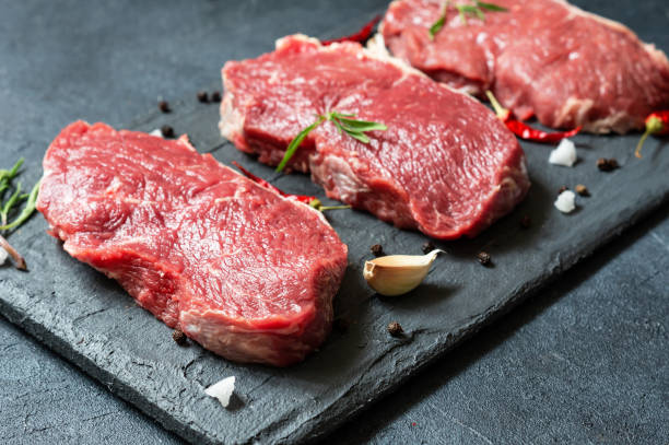 istock Raw beef steak meat on stone board with thyme and peppers, butcher concept 1409869033
