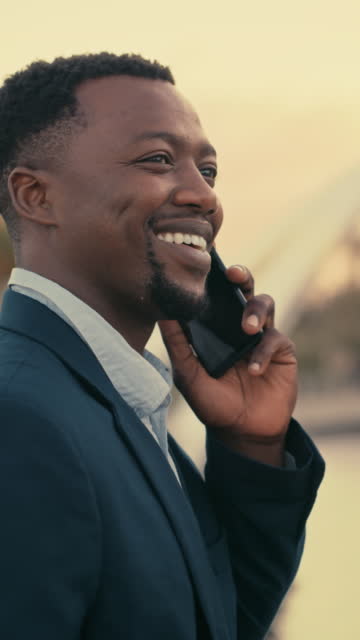 Young smiling business man having conversation on call on a phone while walking in the city. Professional male corporate worker talking and networking with clients while commuting to work in morning