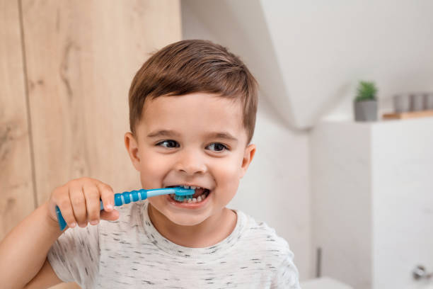 niño cepillándose los dientes. cepillo y pasta de dientes para niños. pequeño bebé divertido cepillándose los dientes en el baño moderno en la mañana soleada. higiene dental y salud de los niños - child human teeth brushing teeth dental hygiene fotografías e imágenes de stock