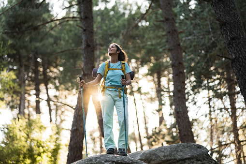 caucasian woman on a rock in the forest is trekking with a backpack