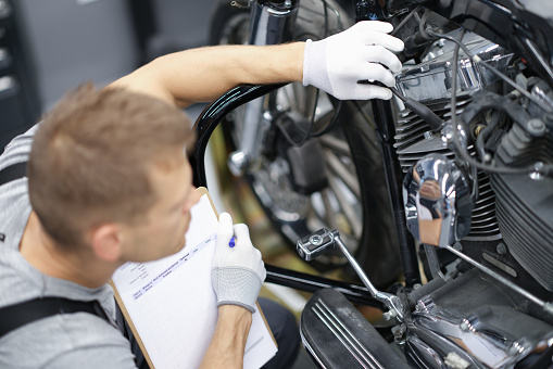 Car mechanic inspects motorcycle breakdowns in car repair shop. Motorcycle maintenance and repair concept