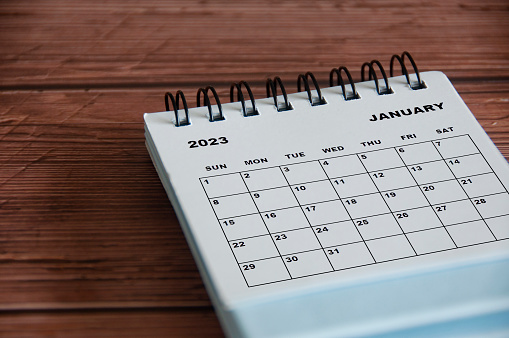 January 2023 white desk calendar on wooden table background. Calendar concept
