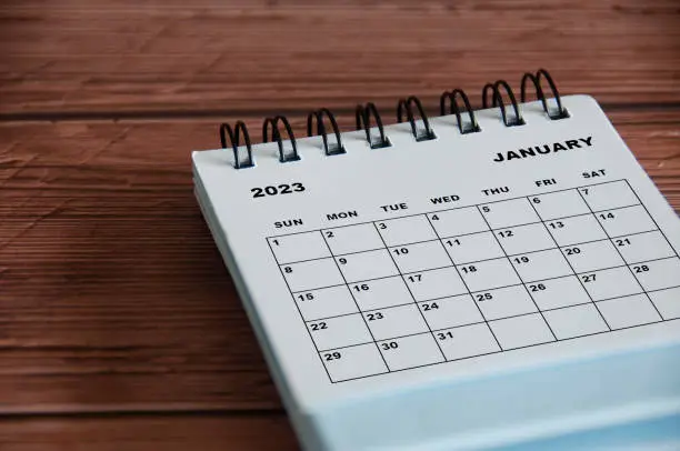 Photo of January 2023 white desk calendar on wooden table background. Calendar concept
