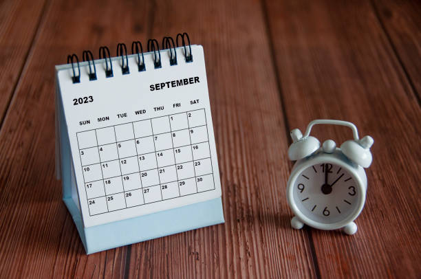 9 월 2023 나무 테이블에 12시를 가리키는 알람 시계가있는 흰색 책상 달력. - 12 oclock 뉴스 사진 이미지