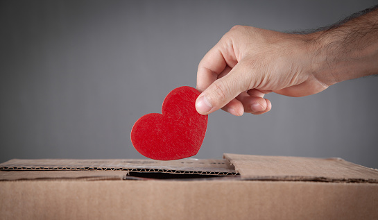 Male hand putting red heart in box.