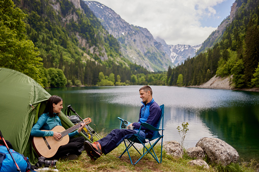 Young couple camping by lake, woman playing guitar