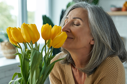 Happy senior woman smelling a bunch of yellow tulips while relaxing at home