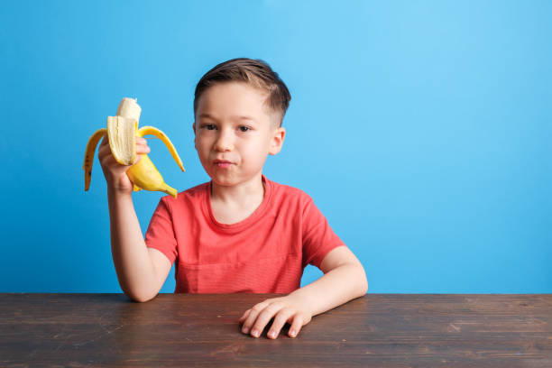 istock Child eating banana on blue background 1409884451