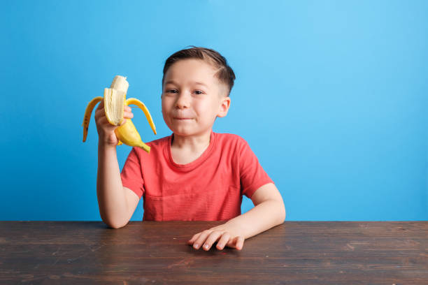 istock Child eating banana on blue background 1409884956