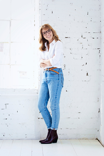 Full length shot of happy woman wearing white shirt and jeans while relaxing at the wall.