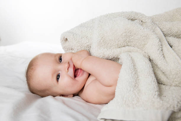 A half-year-old cute baby in a diaper and a towel lies on his back and looks cheerfully at the camera stock photo