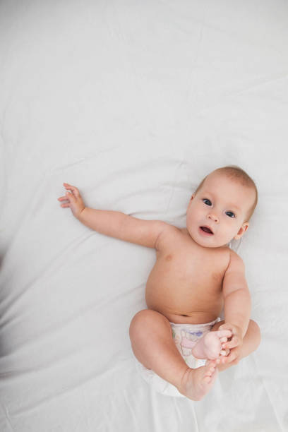 A half-year-old beautiful baby in a diaper lies on his back and looks at the camera with joyful emotions stock photo