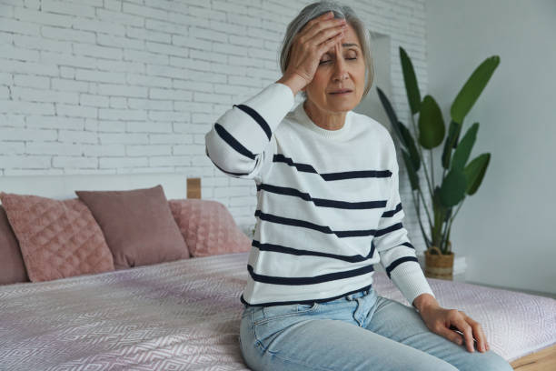 istock Frustrated senior woman touching forehead while sitting on the bed at home 1409887455