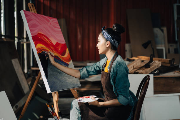 Asian Female Artist Draws create art piece with palette and brush painting at studio. stock photo