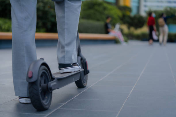 Young Asian freelancer with disposable cup traveling with electric scooter go to public park for work outside.