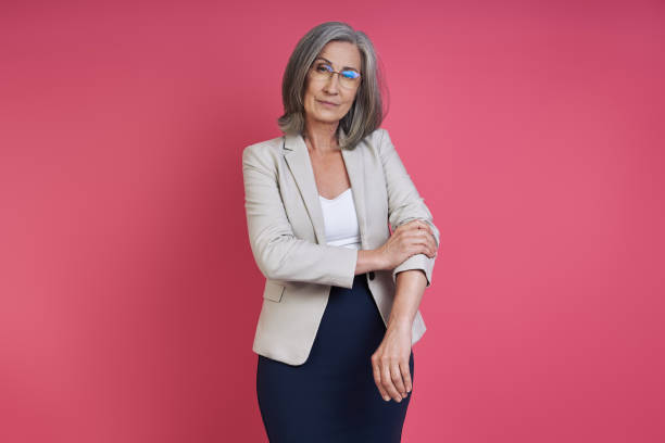 istock Confident senior woman rolling up sleeve on her jacket while standing against pink background 1409889968