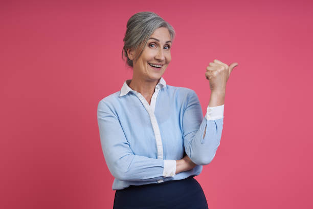 istock Happy senior woman pointing away while standing against pink background 1409890249