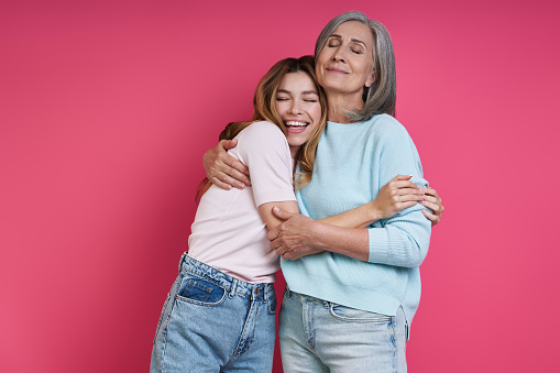 Madre feliz e hija adulta abrazadas sobre fondo rosa photo