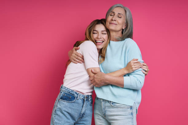 Happy mother and adult daughter embracing against pink background stock photo
