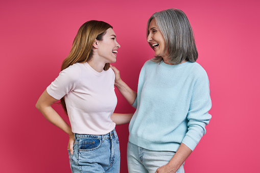 Happy mother and adult daughter looking at each other against pink background