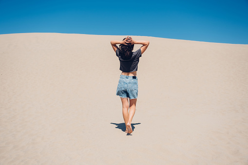 Minimalistic landscape photo of young woman walking in desert. Alon person in a big world. Freedom and happiness concert