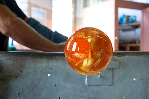 A Murano glass blower is preparing an incandescent globe of glass for blowing it. Focus on the glass.