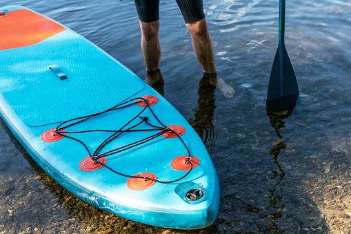 Man faceless with stand up paddleboard blue SUP on the water lake with paddle male legs active lifestyle summer activities