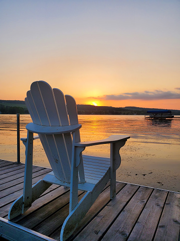 Adirondack chair on a dock on a lake at sunset. Finger Lakes, NY, USA