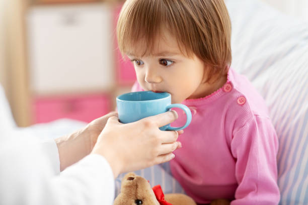 doctor giving hot tea to sick little girl in bed stock photo