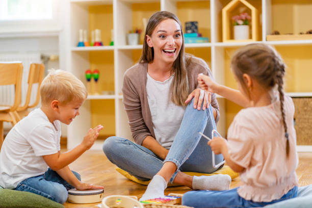 istock Kindergarten teacher with children sitting on the floor having music class, using various instruments and percussion 1409895366