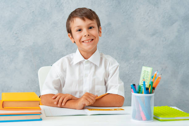 Back to school. Happy smiling student draws at the Desk. A schoolboy solves his homework. A boy from elementary school Back to school. Happy smiling student draws at the Desk. A schoolboy solves his homework. A boy from elementary school. question mark depression sitting asking stock pictures, royalty-free photos & images