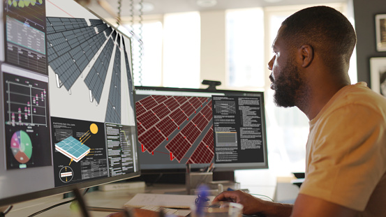 Close up stock image of an African American man working at a computer screen. He’s working on CAD software looking at the design of a solar panel array in CAD with data.