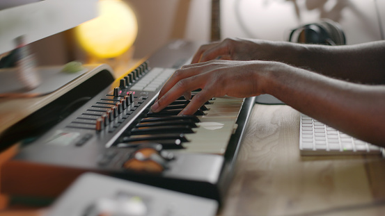 Stock close up image of an Afro Caribbean ( African American ) man playing a musical keyboard in a small recording studio.