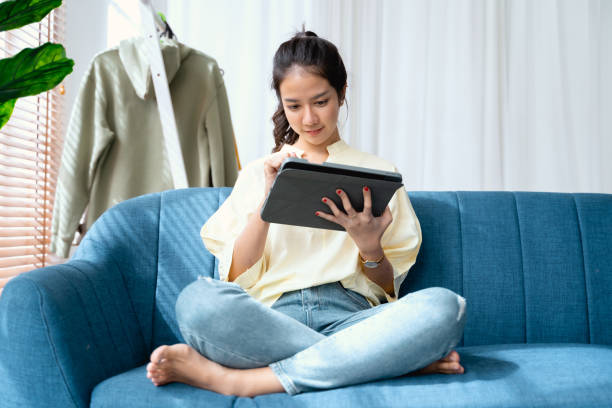 Young Asian woman using tablet and pen on sofa happy and smile.
