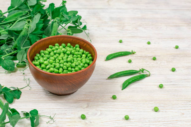 pois verts frais dans un bol sur fond de pousses de pois. - pea pod photos et images de collection