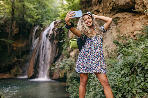 Shot of women taking a selfie in nature. Photo of a beautiful, smiling woman taking a selfie in front of a waterfall.
